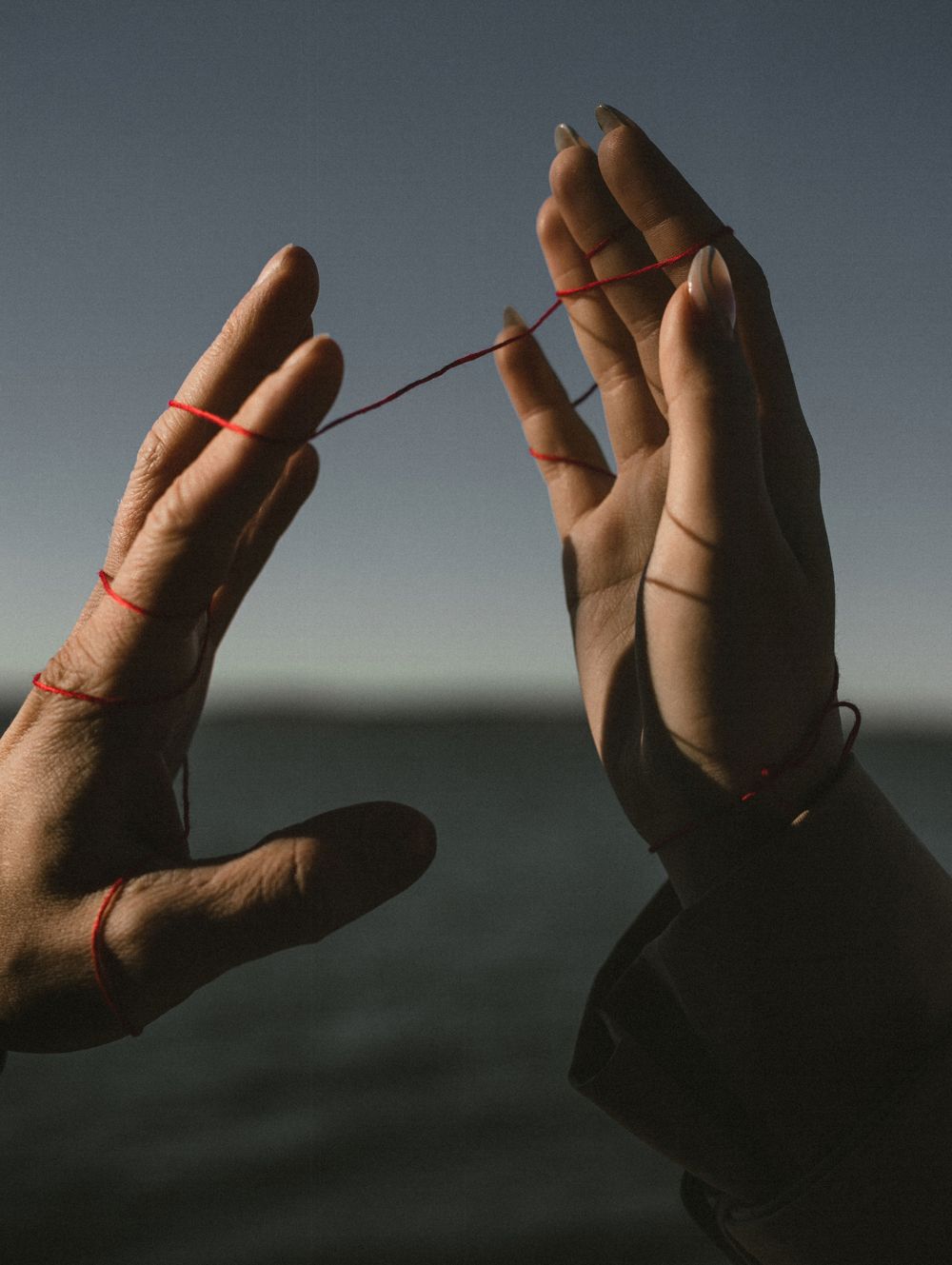 Due mani tengono un filo rosso teso tra le dita