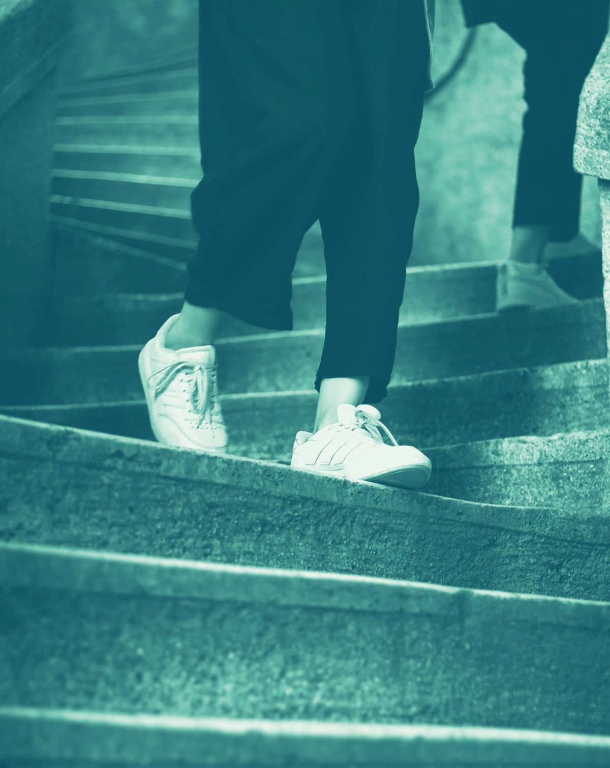 I piedi di una persona con scarpe da ginnastica che sale una scala di pietra, in tonalità verde acqua